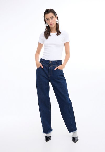 Tricou alb ajustat asortat cu blugi din denim întunecat, cu talie înaltă și tivuri desfăcute, având un design subtil cu etichete țesute.