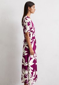 Lila Blumenkleid mit weißen Blattmustern, kurzen Ärmeln und einem Taillengürtel. Das Kleid reicht bis zur Mitte der Wade, hat eine lockere Passform und einen glatten Stoff.