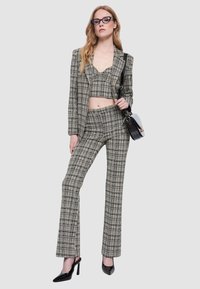 Donna che indossa un blazer grigio a quadri, top corto e pantaloni abbinati, tacchi alti neri, occhiali stile cat-eye e porta una borsa a tracolla bianca e nera.