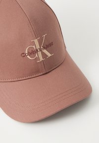 Rózsaszínű sapka texturált anyagból, hímzett CK logóval és világosabb árnyalatú "Calvin Klein Jeans" felirattal. Lapos karimás kialakítás.