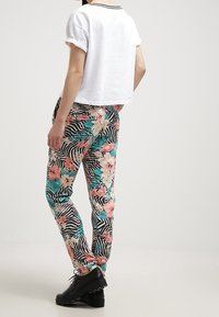 T-shirt blanc court avec manches retroussées, associé à un pantalon à motifs floraux et zèbres en rose, bleu canard et noir, porté avec des chaussures noires.