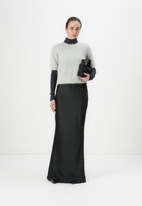 Lichtgrijze fuzzy short-sleeve sweater over een lange zwarte satijnen rok, met een zwarte tas. Gladde texturen en contrasterende kleuren.