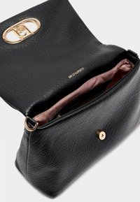 Schwarze handgefertigte Ledertasche mit goldfarbener ovaler Hardware-Applikation, ausgestattet mit einem rosa Innenfutter und einem obenliegenden Magnetverschluss.