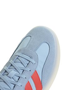Svijetloplavi tenisice s glatkom gornjom površinom i akcentima od antilopa, s crvenim trakama, ravnim vezicama i bijelom gumiranom potplatom.