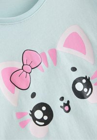 Vaaleansininen puuvillainen t-paita, jossa on sarjakuvamaisen kissan naaman kuva pinkeillä yksityiskohdilla, suurilla silmillä ja yhdellä korvalla oleva pinkki rusetti.