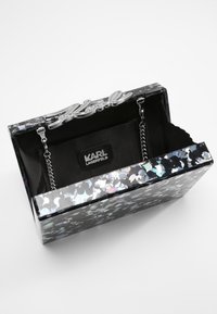 Borsa a mano rettangolare nera con un esterno di paillettes lucide multicolori. Presenta un logo argentato "Karl" e una tracolla a catena interna.