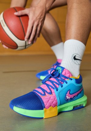 Basketballspiller der dribler, iført farverige Nike-sneakers med blå, pink, turkis og gule accenter, hvide Nike-strømper og holder en orange basketball.