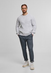 Suéter de punto gris claro con un patrón texturizado, combinado con pantalones oscuros gris ajustados y zapatillas de deporte crema con acentos beige.