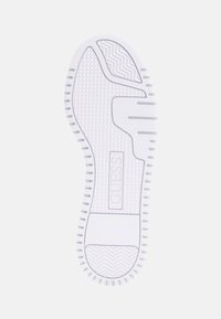 White rubber shoe sole featuring a textured surface, grooves, and a logo in the center, with a herringbone pattern near the toe area.