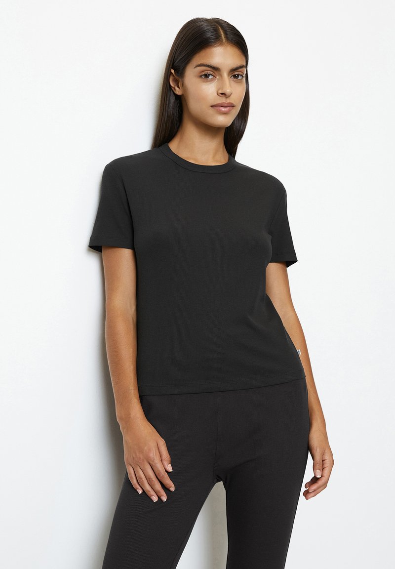 Camiseta negra de canalé con mangas cortas, escote redondo y un corte ajustado, combinada con pantalones negros a juego. Textura de tela suave.