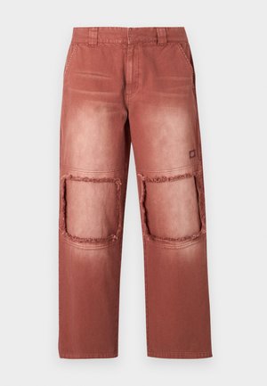 Roostes värvitud püksid, millel on pleekinud tekstuur, kus on kaks suurt, kulunud lõikekohta põlvedel ning tavad taskud.