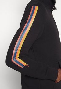 Felpa nera con zip e finitura testurizzata, caratterizzata da accenti multicolore a strisce blu, giallo, rosa e rosso lungo le maniche.
