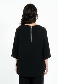 Top nero con maniche a tre quarti, caratterizzato da una zip argentata sul retro. Tessuto liscio, orlo arrotondato, design minimale.