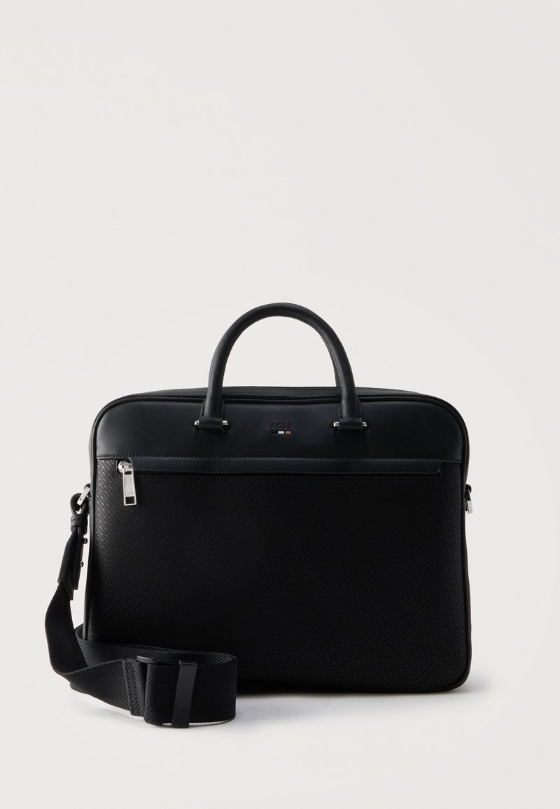 Μαύρη δερμάτινη τσάντα χειρός με πάνω χερούλια, μπροστινή τσέπη με φερμουάρ και ρυθμιζόμενο ιμάντα ώμου σε απλό λευκό φόντο.