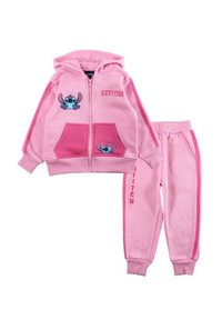 Ensemble de surv êtement rose en deux pièces comprenant un sweat à capuche zippé avec des motifs Stitch et des poches, accompagné d'un pantalon assorti avec un détail de marque sur le côté.