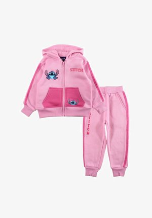 Ensemble de survêtement rose en deux pièces comprenant un sweat à capuche zippé avec des motifs Stitch et des poches, accompagné d'un pantalon assorti avec un détail de marque sur le côté.