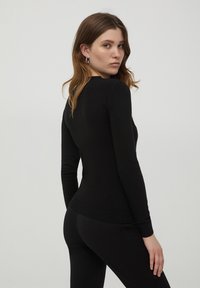 Maglietta nera a maniche lunghe, aderente, realizzata in un tessuto a maglia liscio, con scollatura a girocollo e orlo a costine, caratterizzata da un design essenziale e dettagli minimi.