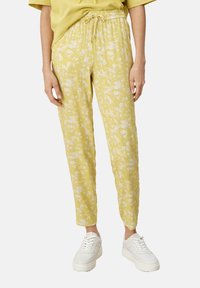 Gule blomstrede bukser med elastisk talje og snøre; letvægtsstof med løs pasform, parret med hvide sneakers.