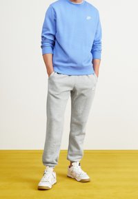 Sudadera Nike de color azul claro con puños acanalados, combinada con pantalones de chándal grises con puños elásticos y zapatillas blancas con acentos beige.