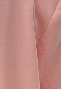Detailní záběr na měkkou růžovou látku s viditelnou diagonální texturou tkaní a prošívaným švem.