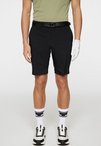 Czarne szorty o prostym kroju, zestawione z zieloną koszulą i czarnym paskiem. Biała rękawiczka na ręce, czarno-białe trampki i białe skarpety.