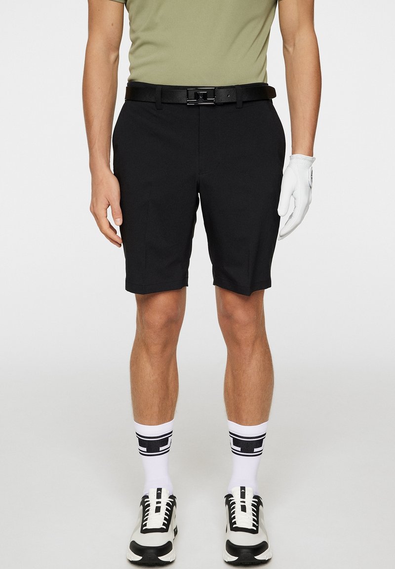 Czarne szorty o prostym kroju, zestawione z zieloną koszulą i czarnym paskiem. Biała rękawiczka na ręce, czarno-białe trampki i białe skarpety.