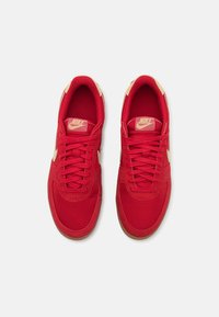 Sarkani Nike kedu ar acs un zamšas augšdaļu, plakaniem šņorēm, brūnām akcentiem un gumijas zoli. Ikonisks logo uz mēles un sāniem.