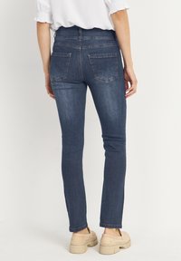 Tight jeans i mörkblå denim har en hög midja, bakfickor och en mjuk textur, i kombination med ljusa skor.