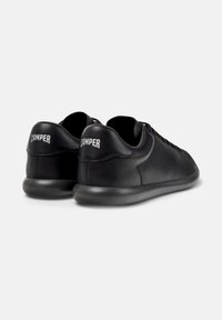 Black sneakers facing right, featuring a smooth leather exterior and a cushioned sole. "Camper" logo displayed on the heel.
