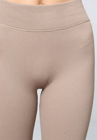 Collants beiges côtelés avec une taille haute, offrant un ajustement près du corps et une texture lisse et extensible.