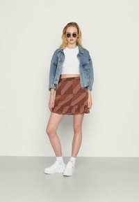 Casaco de ganga sobre um top cortado branco, combinado com uma saia mini estampada castanha com bainha rodada e sapatilhas brancas de plataforma.