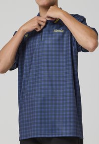 Polo majica s kratkim rukavima u plavom karo uzorku sa žutim naglascima. Ovratnik s gumbima, ležerni kroj i mekana tekstura. Ima izvezeni logo "Riviera".