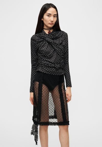 Μαύρο τοπ με πουά σχέδιο και πιέτες, συνδυασμένο με διαφανής μαύρη πουά φούστα με βολάν. Συμπεριλαμβάνεται κολιέ τύπου τσοκέρ.