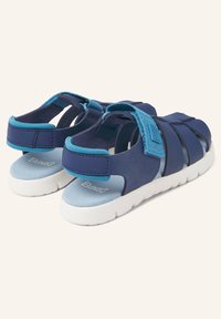 Siniset sandaalit, joissa on teksturoitu päällinen, hihnalukot ja pehmustettu pohja. Ominaisuuksiin kuuluu tumman ja vaalean sinisen sävyjen yhdistelmä. Valkoinen kumipohja.