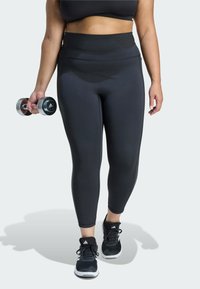 Black high-waisted leggings made from stretch fabric, paired with black athletic shoes, held dumbbell in hand, featuring a smooth texture.