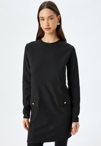 Abito nero a coste con maniche lunghe, scollo a girocollo, due tasche frontali e bottoni dorati. Texture liscia e silhouette aderente.