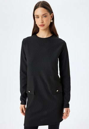 Schwarzes, geripptes Kleid mit langen Ärmeln, Rundhalsausschnitt, zwei vorderen Taschen und goldfarbenen Knöpfen. Glatte Textur und figurschmeichelnde Silhouette.