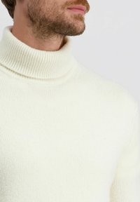 Witte coltrui met een geribbeld textuur, met een hoge hals en een aansluitend ontwerp. De stof lijkt zacht en comfortabel.