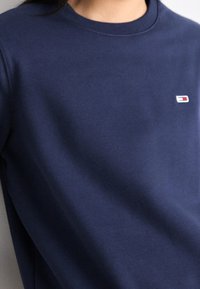 Felpa blu navy realizzata in materiale morbido con scollatura rotonda. Presenta un piccolo logo a marchio sul lato sinistro del petto. Texture liscia.