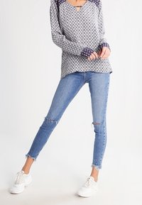 T-shirt a maniche lunghe con motivo che presenta un design navy e bianco, abbinato a jeans skinny azzurri chiari con ginocchia strappate e orli sfrangiati.