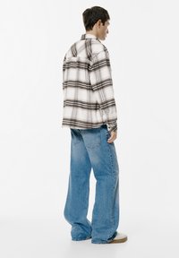 Camicia di flanella a quadri bianca e nera con vestibilità comoda, abbinata a jeans a gamba larga azzurri e sneaker beige.