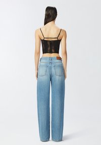 Crni čipkani korzet s tankim trakama, uparen s visokim svotovima svijetloplavih širokih traperica koje imaju stražnje džepove i kožnu oznaku na pojasu.