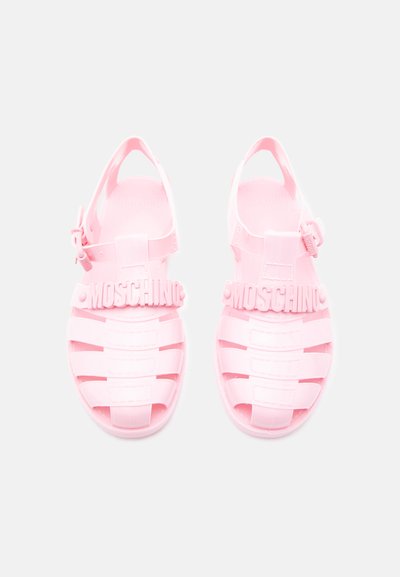 Paire de sandales en plastique rose avec des brides tissées, des boucles à la cheville et un lettrage "MOSCHINO" en relief sur les brides supérieures.
