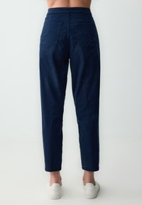 Marineblauwe denimbroek met een hoge taille, taps toelopende pijpen, twee achterzakken en een nette afwerking. Draagt met witte sneakers.