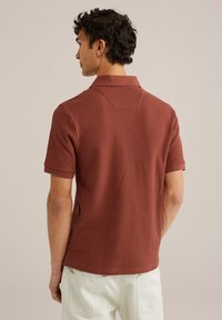 Rust-colored polo shirt with a textured pattern, short sleeves, and a classic collar, shown from the back against a neutral background.