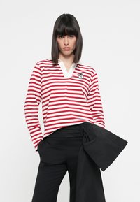 Rot und weiß gestreiftes Langarmshirt mit V-Ausschnitt und gesticktem Design. Kombiniert mit hoch taillierten schwarzen Hosen mit gebundenem Bund.