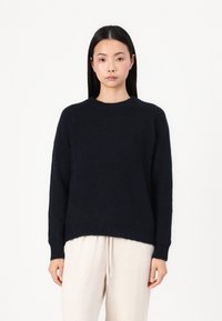 Navy sweater made of soft knit material, featuring a crew neckline and long sleeves with ribbed cuffs, paired with light beige trousers.