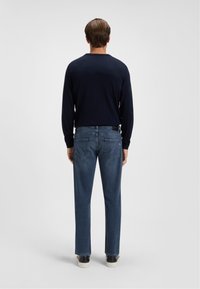 Navy blue sweater with a crew neck, paired with light blue jeans featuring back pockets. Model wears dark sneakers.