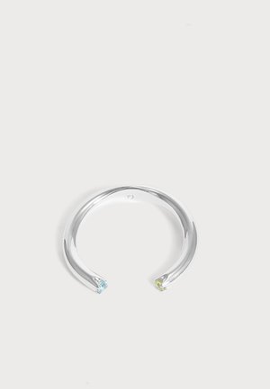 Pulsera abierta de plata con diseño retorcido, que presenta una pequeña piedra preciosa azul en un extremo y una piedra preciosa amarilla en el otro.