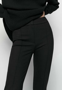 Czarne, dopasowane spodnie wykonane z gładkiego materiału, cechujące się wysokim stanem, prostymi liniami i minimalnymi detalami przeszyć, zaprojektowane z myślą o dopasowanej sylwetce.